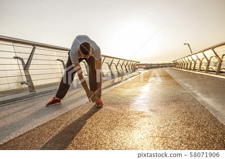 Young man stretching his leg muscles outside Young man stretching his leg muscles outside 58071906