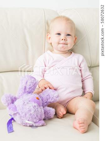 childhood, babyhood and people concept - happy little baby girl sitting on couch at home 58072632
