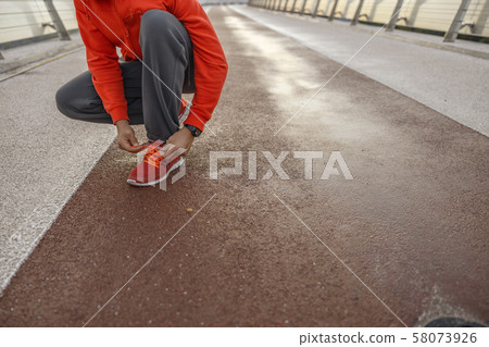 Athletic man bending over an untied shoelace 58073926