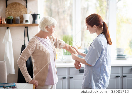 Caring red-haired nurse putting gel on arm for woman Caring red-haired nurse putting gel on arm for woman 58081713
