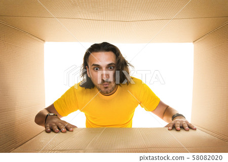 Young man opening the biggest postal package isolated on white Young man opening the biggest postal package isolated on white 58082020