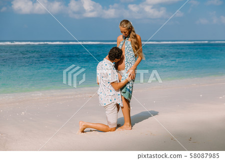 Young pregnant woman with husband relaxing at paradise beach. Happy couple in tropics Young pregnant woman with husband relaxing at paradise beach. Happy couple in tropics 58087985