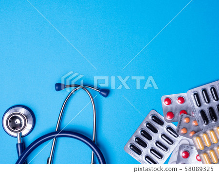 Top view with a stethoscope and blisters with multicolored pills on a blue background Top view with a stethoscope and blisters with multicolored pills on a blue background 58089325