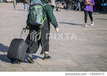Unrecognizable young girl walking in the street with backpack and suitcase, travel and tourism 58089573