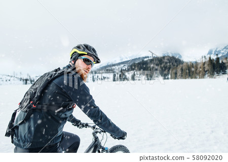 Side view of mountain biker riding in snow outdoors in winter nature. 58092020