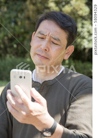 Senior man thinking while looking at smartphone screen in Yoyogi Park 58094329