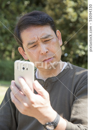 Senior man thinking while looking at smartphone screen in Yoyogi Park 58094330