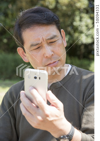 Senior man thinking while looking at smartphone screen in Yoyogi Park 58094331