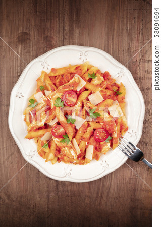 Penne pasta with chicken, tomato sauce and parsley, shot from the top on a dark rustic wooden Penne pasta with chicken, tomato sauce and parsley, shot from the top on a dark rustic wooden 58094694