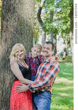 Beautiful happy young family hugs by a tree in the Beautiful happy young family hugs by a tree in the 58097044
