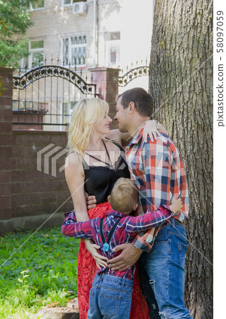 Beautiful happy young family hugs by a tree in the Beautiful happy young family hugs by a tree in the 58097059