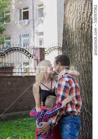 Beautiful happy young family hugs by a tree in the Beautiful happy young family hugs by a tree in the 58097062