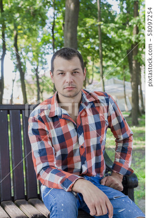 Young handsome man sits on a bench in a park. Young handsome man sits on a bench in a park. 58097254