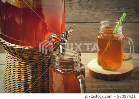 Fresh homemade Kombucha fermented tea drink in jar with faucet and in cans-mugs on wooden background Fresh homemade Kombucha fermented tea drink in jar with faucet and in cans-mugs on wooden background 58097421