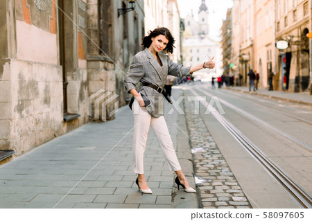 Young sexy woman in white pants and jacket hailing a taxi standing on the road, young female with 58097605