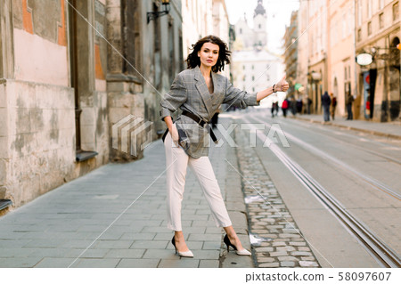 Image of brunette woman in stylish business clothes stopping taxi or car in the city street Image of brunette woman in stylish business clothes stopping taxi or car in the city street 58097607
