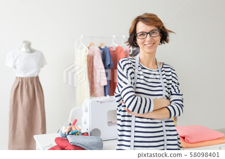 Portrait of a positive young woman seamstress cutter standing on the background of her desktop with 58098401