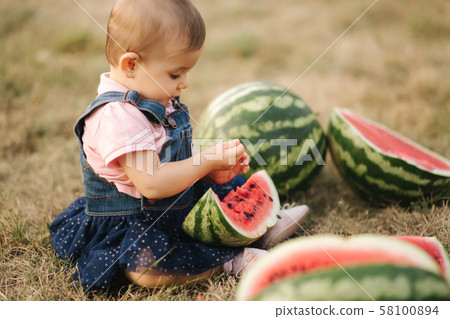 Cute little baby girl laughing with watermelons. Girl dressed in denim dress. Summer portrait of 58100894