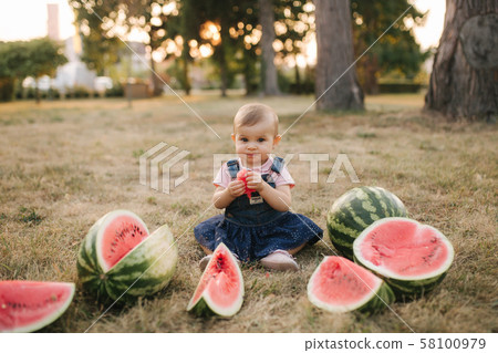 Cute little baby girl laughing with watermelons. Girl dressed in denim dress. Summer portrait of Cute little baby girl laughing with watermelons. Girl dressed in denim dress. Summer portrait of 58100979