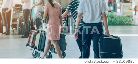 Passengers with big roller luggage stand to wait for the car to pick up at airport arrival terminal. 58109883