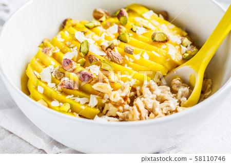 Oatmeal with mango and nuts in white bowl. Oatmeal with mango and nuts in white bowl. 58110746