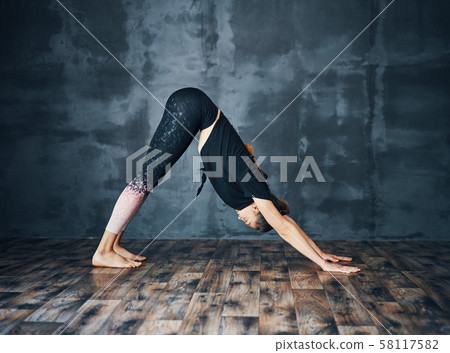 Young attractive woman practicing yoga standing in downward facing dog asana adho mukha svanasana 58117582