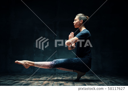 Young beautiful woman doing yoga asana tiptoe pose prapadasana variation on dark room Young beautiful woman doing yoga asana tiptoe pose prapadasana variation on dark room 58117627