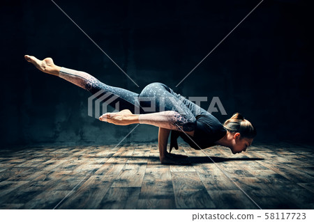 Young woman practicing yoga doing hurdler pose in dark room Young woman practicing yoga doing hurdler pose in dark room 58117723