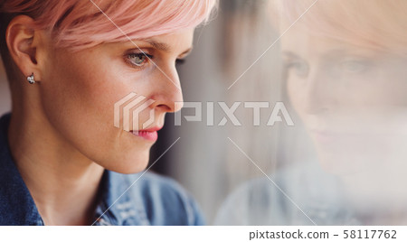 A close-up portrait of young attractive woman standing by window at home. 58117762