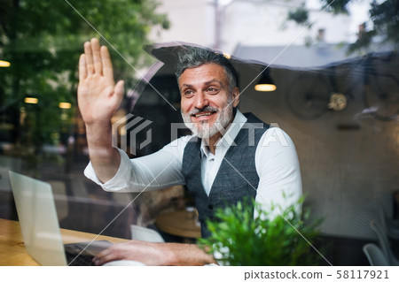 Mature man with laptop at the table in a cafe, greeting somebody. Mature man with laptop at the table in a cafe, greeting somebody. 58117921