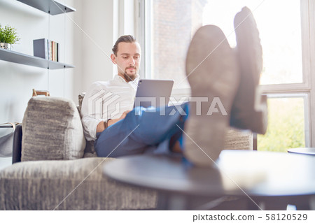 Image of businessman sitting on sofa with tablet in his hands in room. Image of businessman sitting on sofa with tablet in his hands in room. 58120529