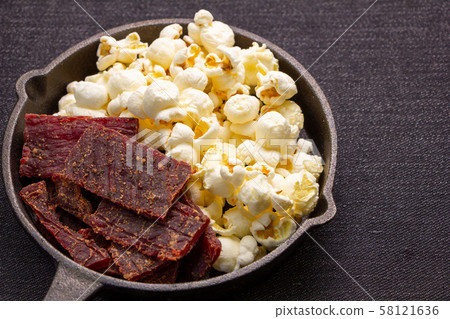 Assorted snacks on skillet. Popcorn and beef jerky. 58121636