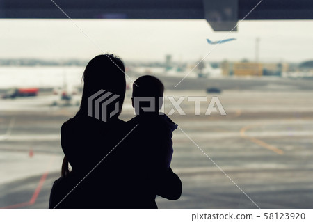 Silhouette of mother holding on hands little toddler boy with window of airport on background 58123920