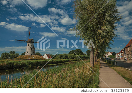 Canal with old windmill and woods next to sidewalk at Damme 58125579