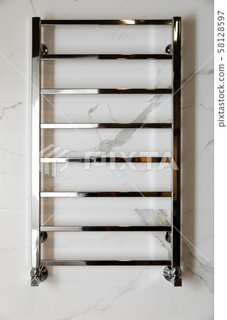 Modern heated towel rail hanging on marble tiled bathroom wall front view Modern heated towel rail hanging on marble tiled bathroom wall front view 58128597