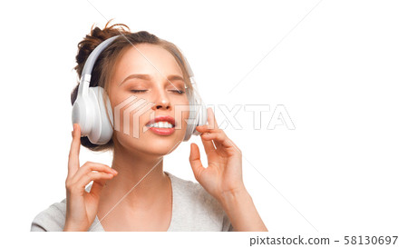 Attractive girl with closed eyes listening to the music via headphones on white background. Sound 58130697