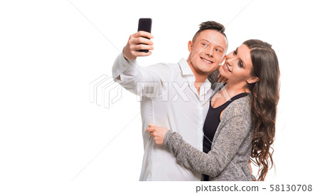 Young couple hugging and smiling while making selfie, standing over white isolated background. 58130708