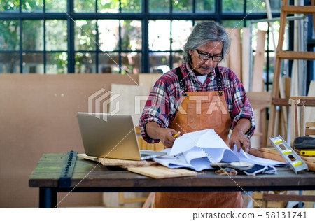 Old Asian craftsman stand in front of laptop and thinking about his process for working Old Asian craftsman stand in front of laptop and thinking about his process for working 58131741