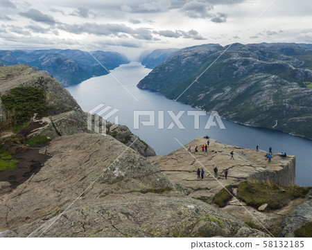 Preikestolen massive cliff at fjord Lysefjord, famous Norway viewpoint with group of tourists and Preikestolen massive cliff at fjord Lysefjord, famous Norway viewpoint with group of tourists and 58132185