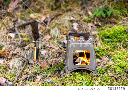 Burning foldable wood stove designed for cooking outdoors using twigs as fuel on nature background 58138659