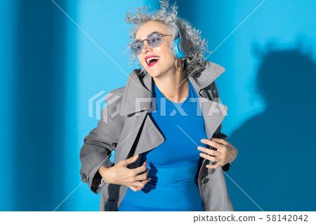 Woman wearing grey coat laughing while listening to earphones 58142042