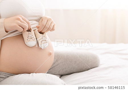Expectant lady holding tiny booties near her belly 58146115
