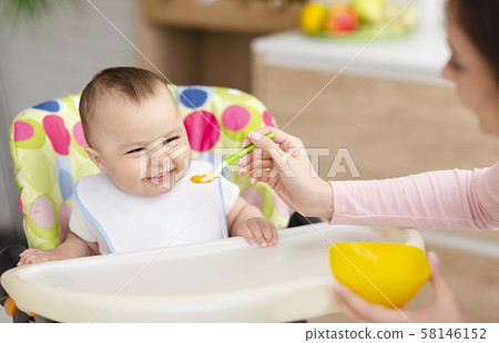 Cheerful baby eating in kitchen in high chair 58146152