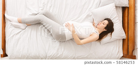 Tired pregnant woman resting in bed, touching her belly 58146253