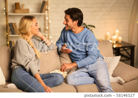 Cute couple talking and eating popcorn in cozy room Cute couple talking and eating popcorn in cozy room 58146327