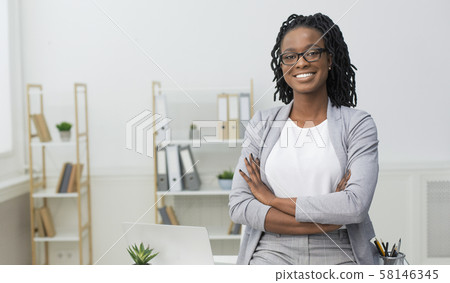 Smiling Black Businesswoman Sitting On Desk In Modern Office Smiling Black Businesswoman Sitting On Desk In Modern Office 58146345