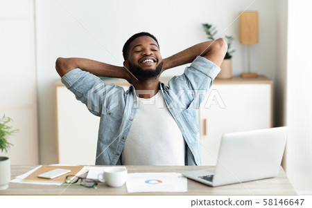 Cheerful employee sitting with hands behind head, relaxing in office 58146647