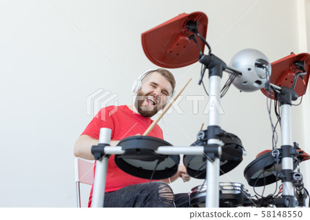 Drummer, hobbies and music concept - young man drummer in red shirt playing the electronic drums Drummer, hobbies and music concept - young man drummer in red shirt playing the electronic drums 58148550