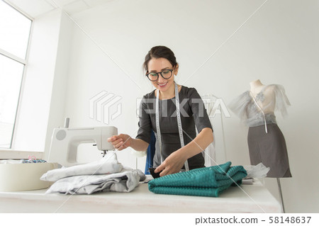 Dressmaker, fashion designer, tailor and people concept - Portrait of a seamstress at work in her Dressmaker, fashion designer, tailor and people concept - Portrait of a seamstress at work in her 58148637