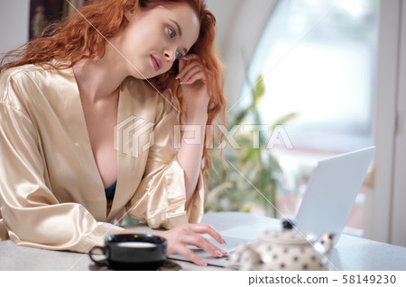Woman in a bathrobe works on a laptop at home Woman in a bathrobe works on a laptop at home 58149230
